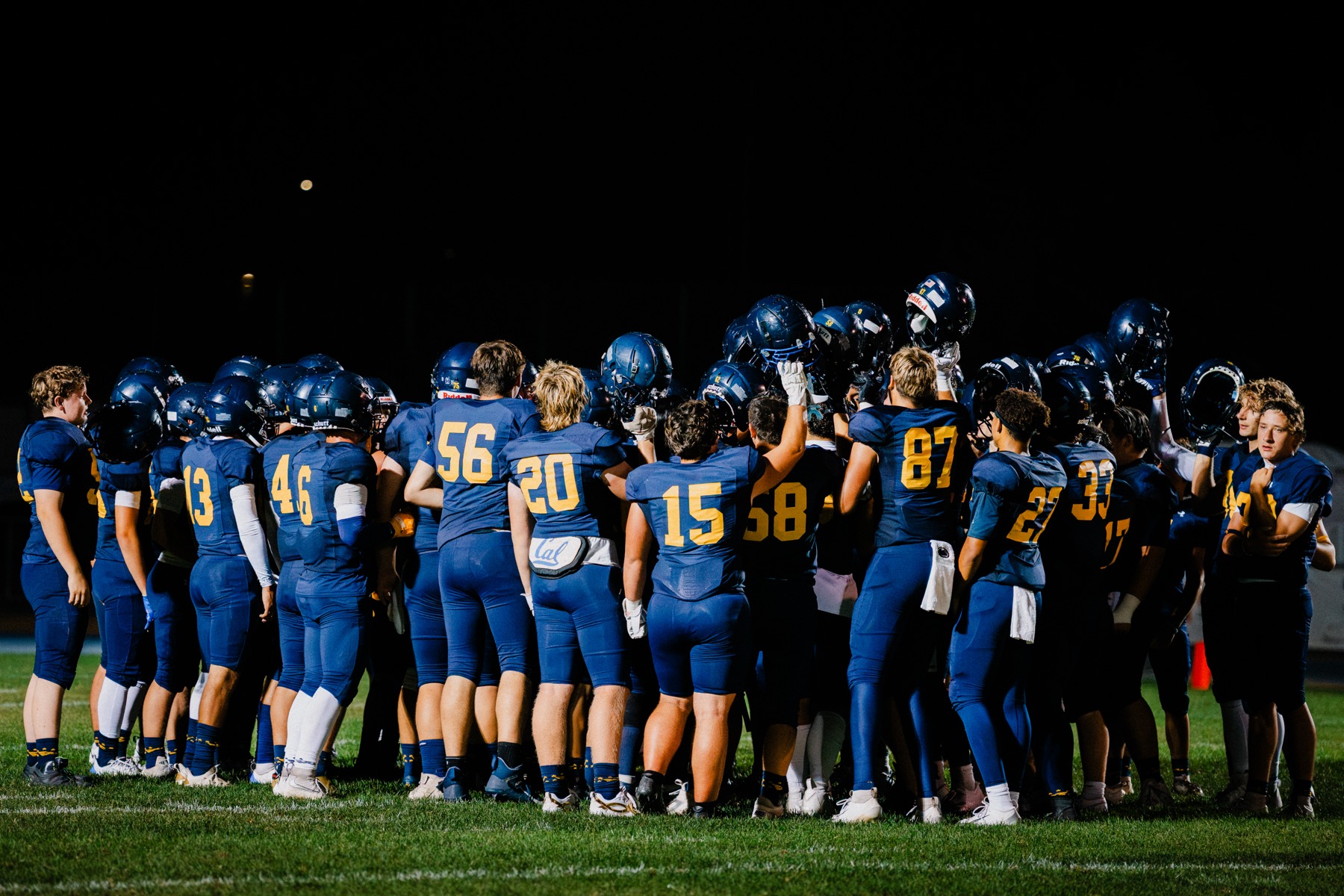 Arroyo Grande's team huddles together with helmets raised under the lights