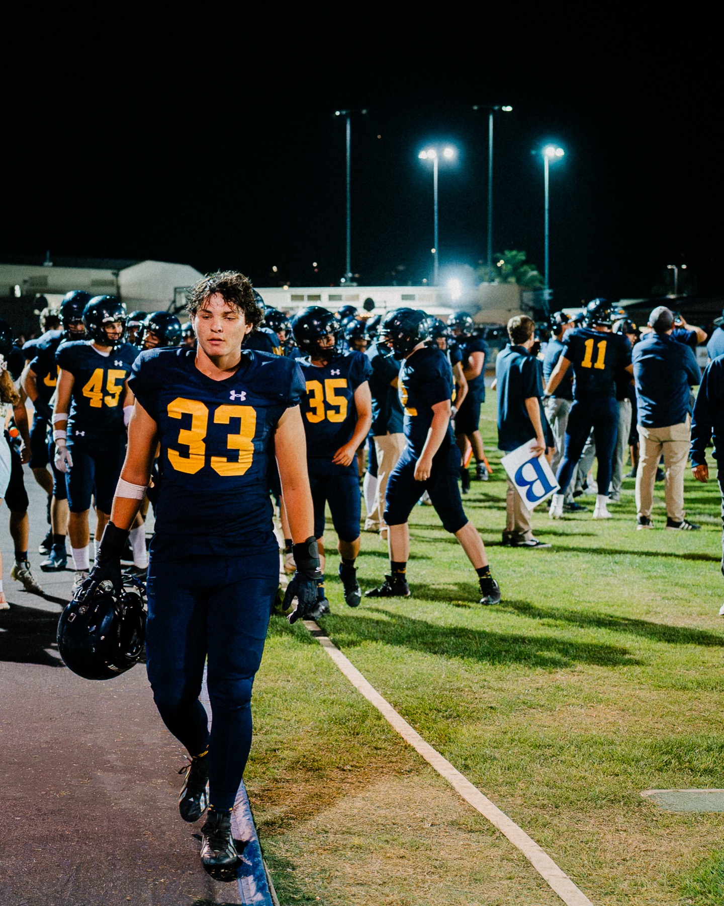 An Arroyo Grande player walks off the field, helmet in hand, during the game