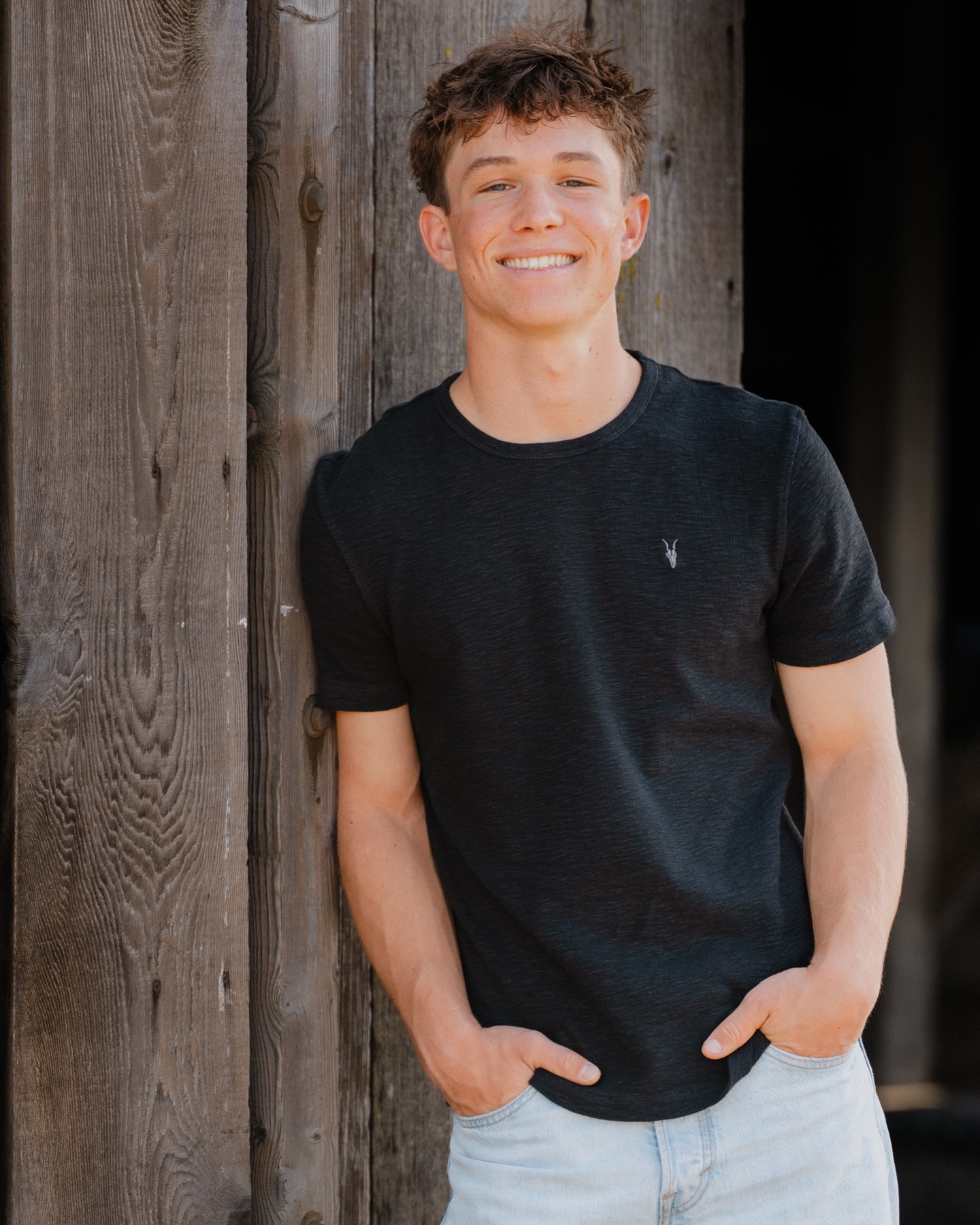 Senior smiling, leaning against a weathered barn door — Central Coast senior photographer