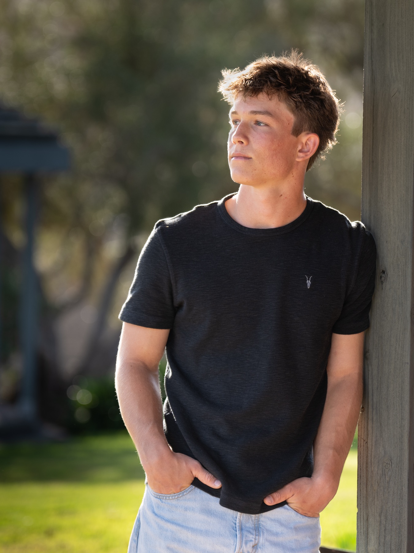 Senior in profile, leaning on a post in backlit golden light — Central Coast senior photographer