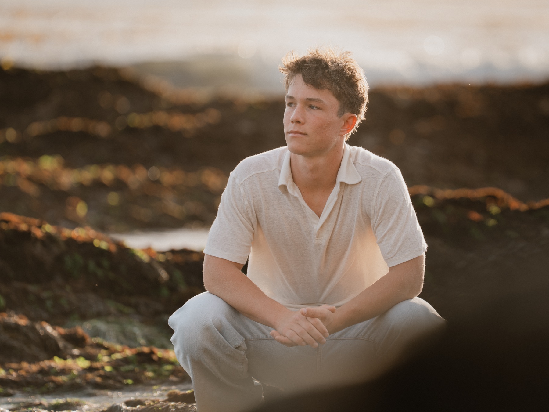 Senior crouching on coastal rocks in warm sunset light — Central Coast senior photographer