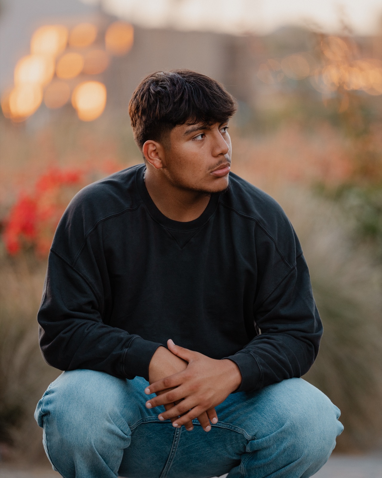 Senior crouching in a black sweatshirt, looking off camera with warm sunset bokeh — Central Coast senior photographer