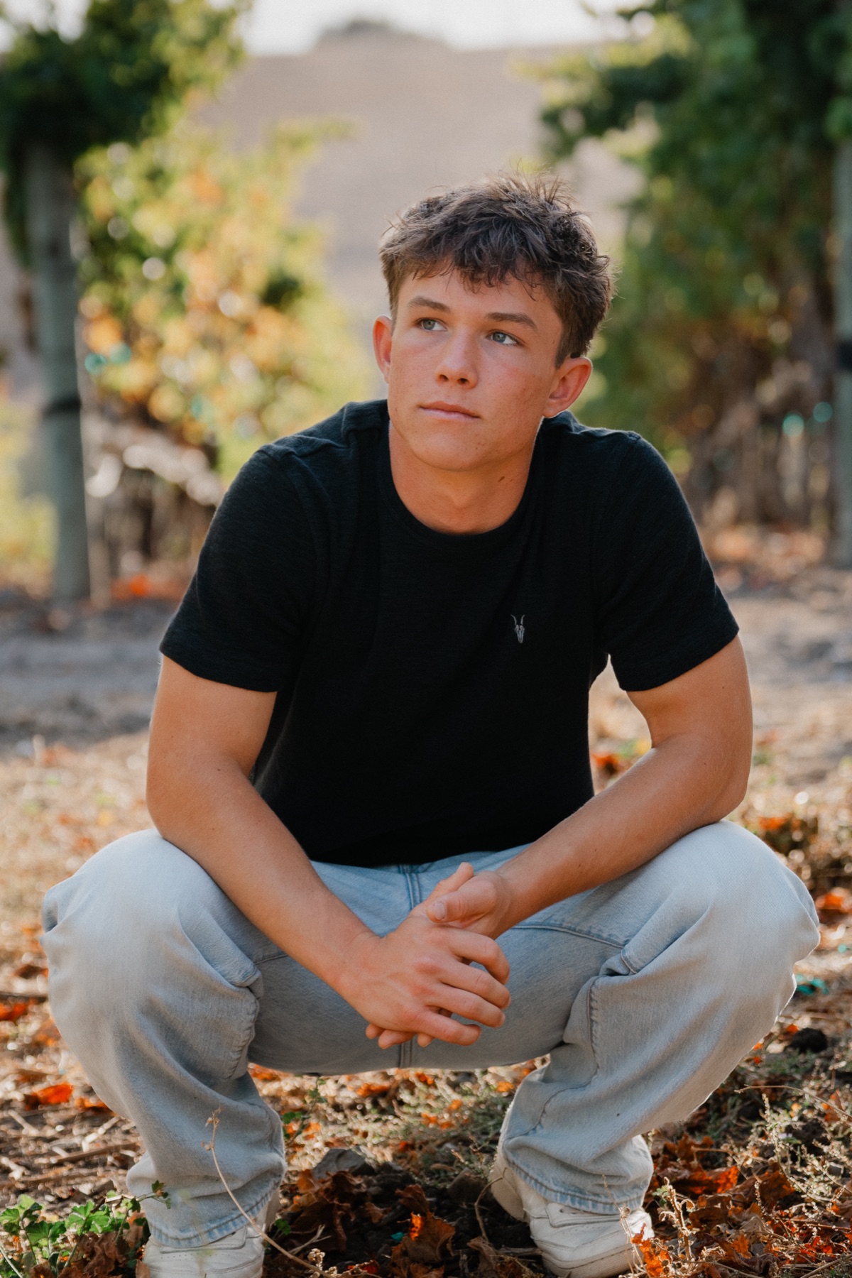 Senior crouching in the vineyard, looking off camera — Central Coast senior photographer