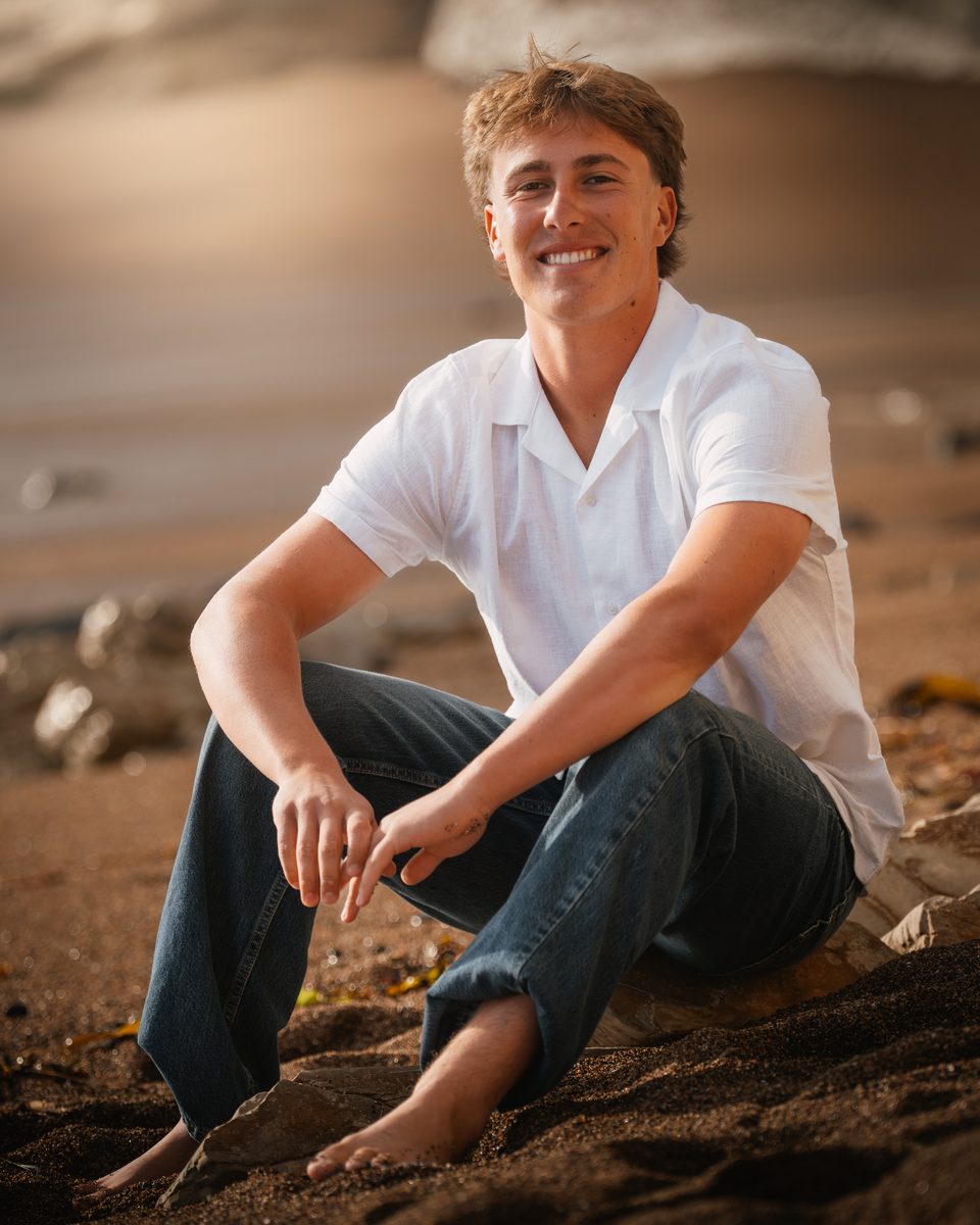 Senior boy sitting relaxed on the beach at golden hour, Central Coast California