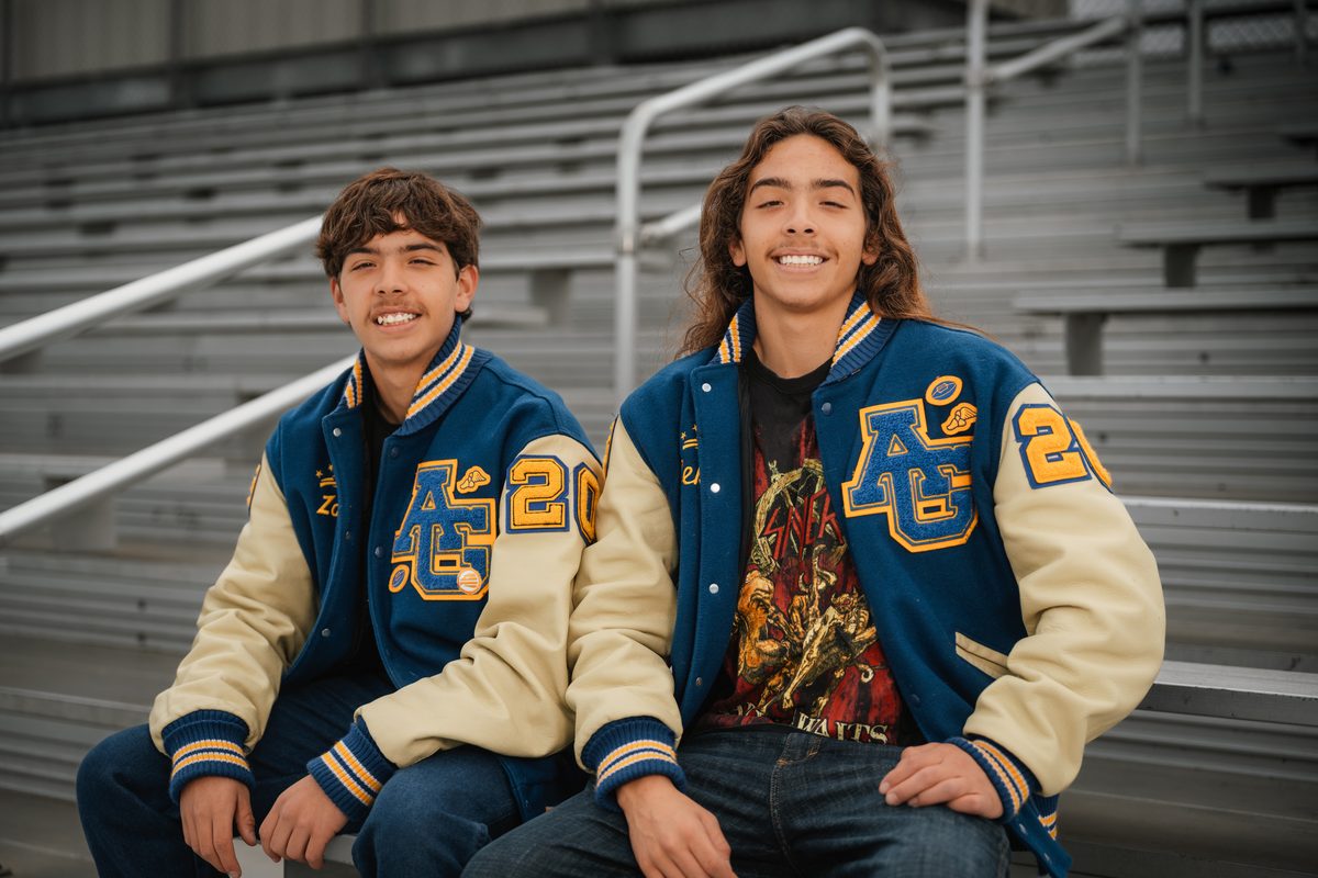 Two brothers in letterman jackets laughing in the bleachers