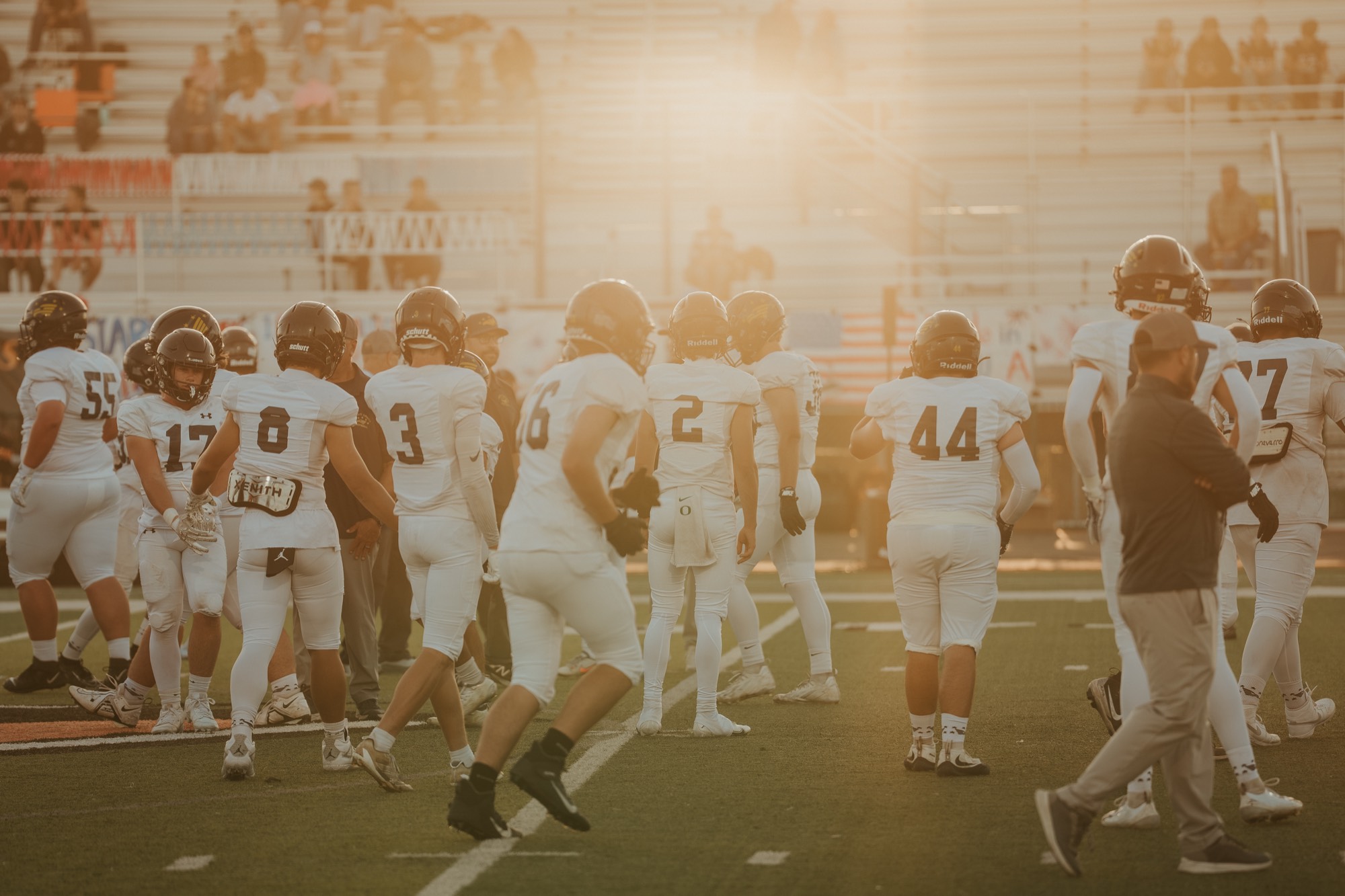 Arroyo Grande football team huddled together on the sideline in golden evening light
